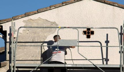 Personne sur un échafaudage en train de réparer le stuc sur le mur extérieur d'un bâtiment ; trou dans le stuc.