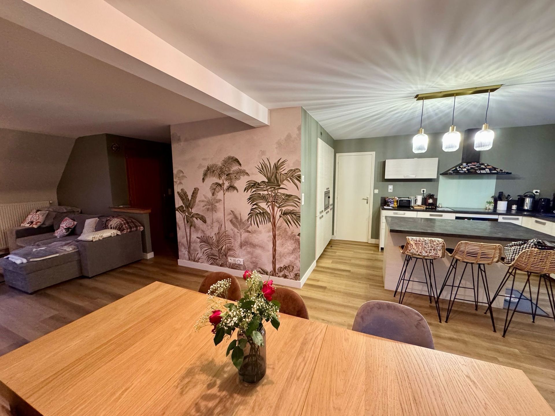 Cuisine ouverte et espace de vie avec table à manger, canapé et papier peint botanique.