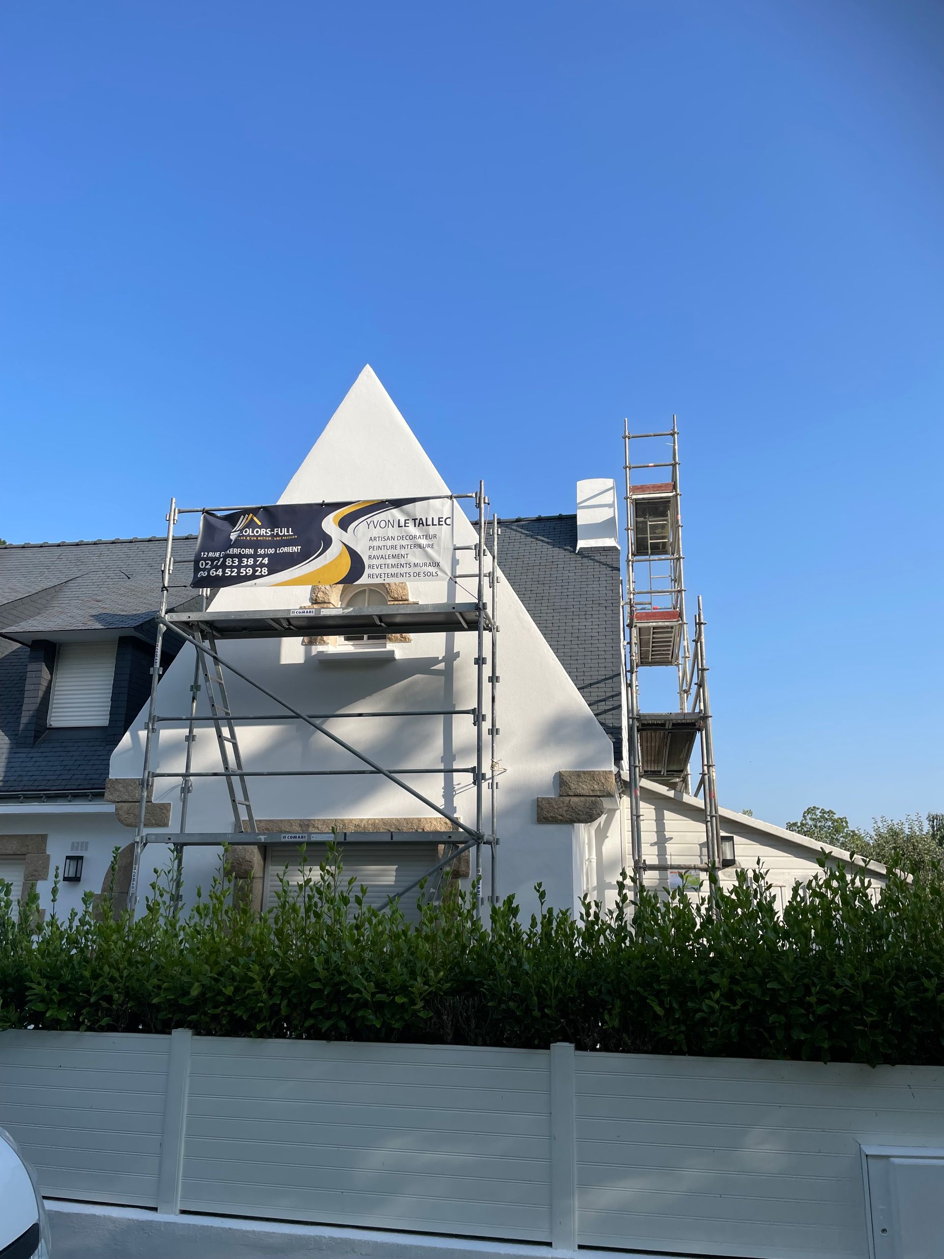 Maison blanche en construction, échafaudage sur le toit, ciel bleu.