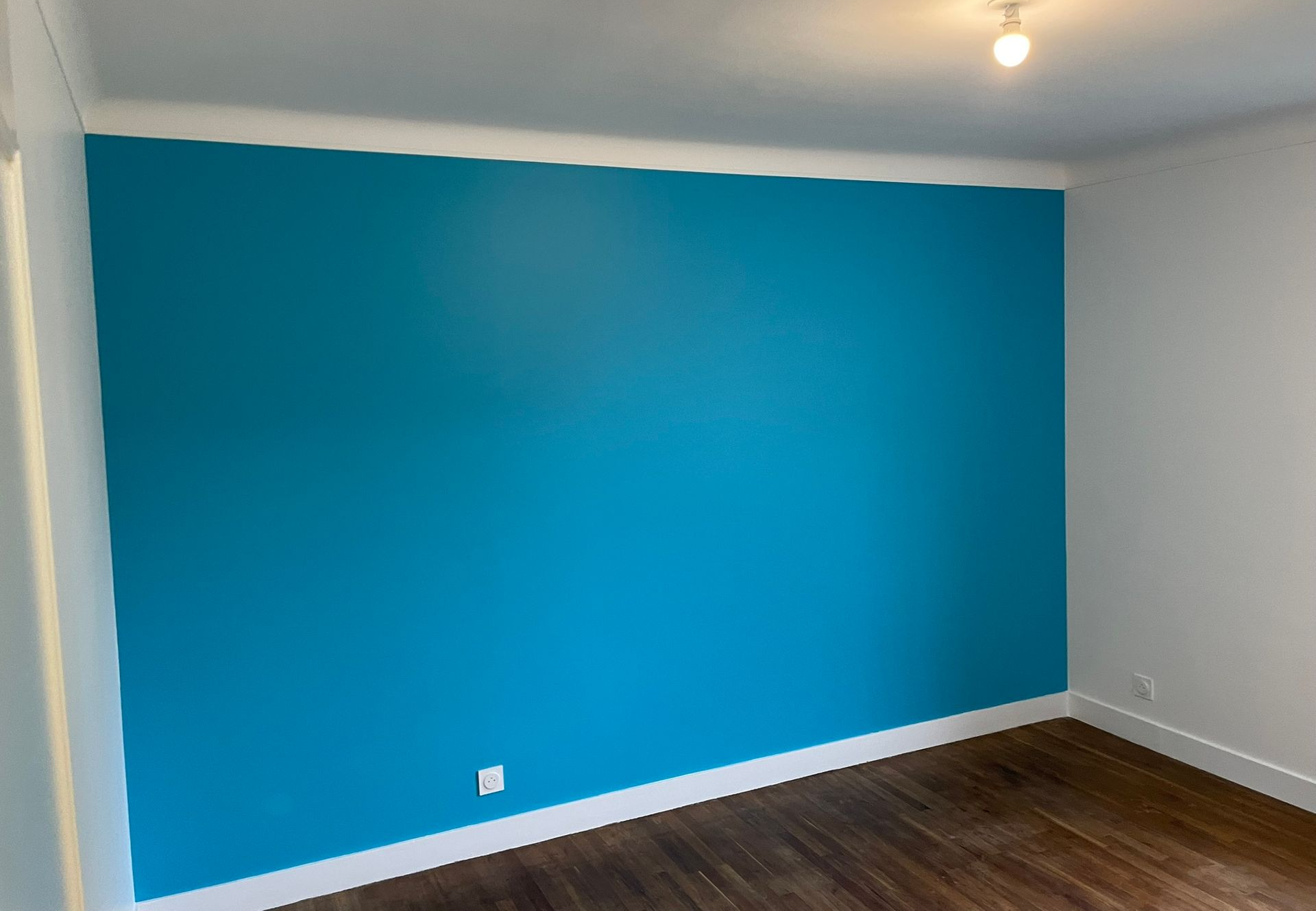 Mur d'accent bleu dans une pièce avec des garnitures blanches et du parquet.
