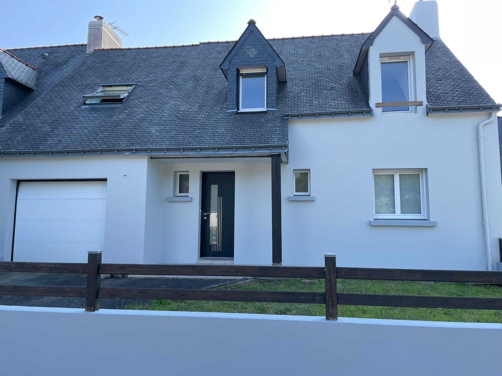Maison blanche avec toit gris, porte noire et petite clôture.