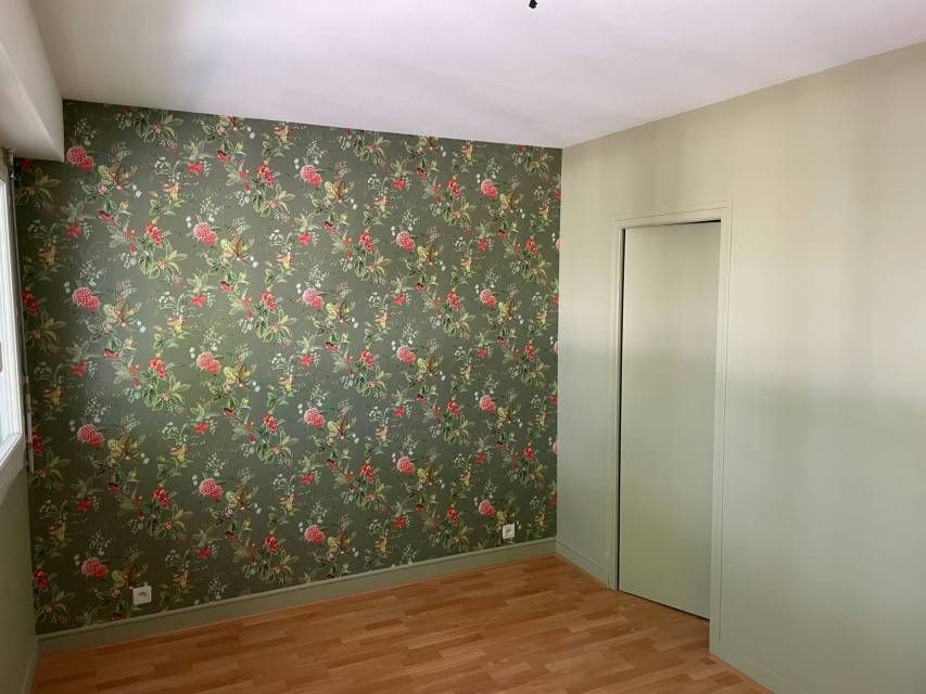 Chambre avec papier peint fleuri sur un mur, murs verts et porte fermée.