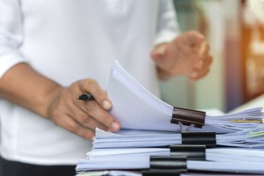 Des mains feuilletant une pile de documents maintenus par des pinces sur un bureau
