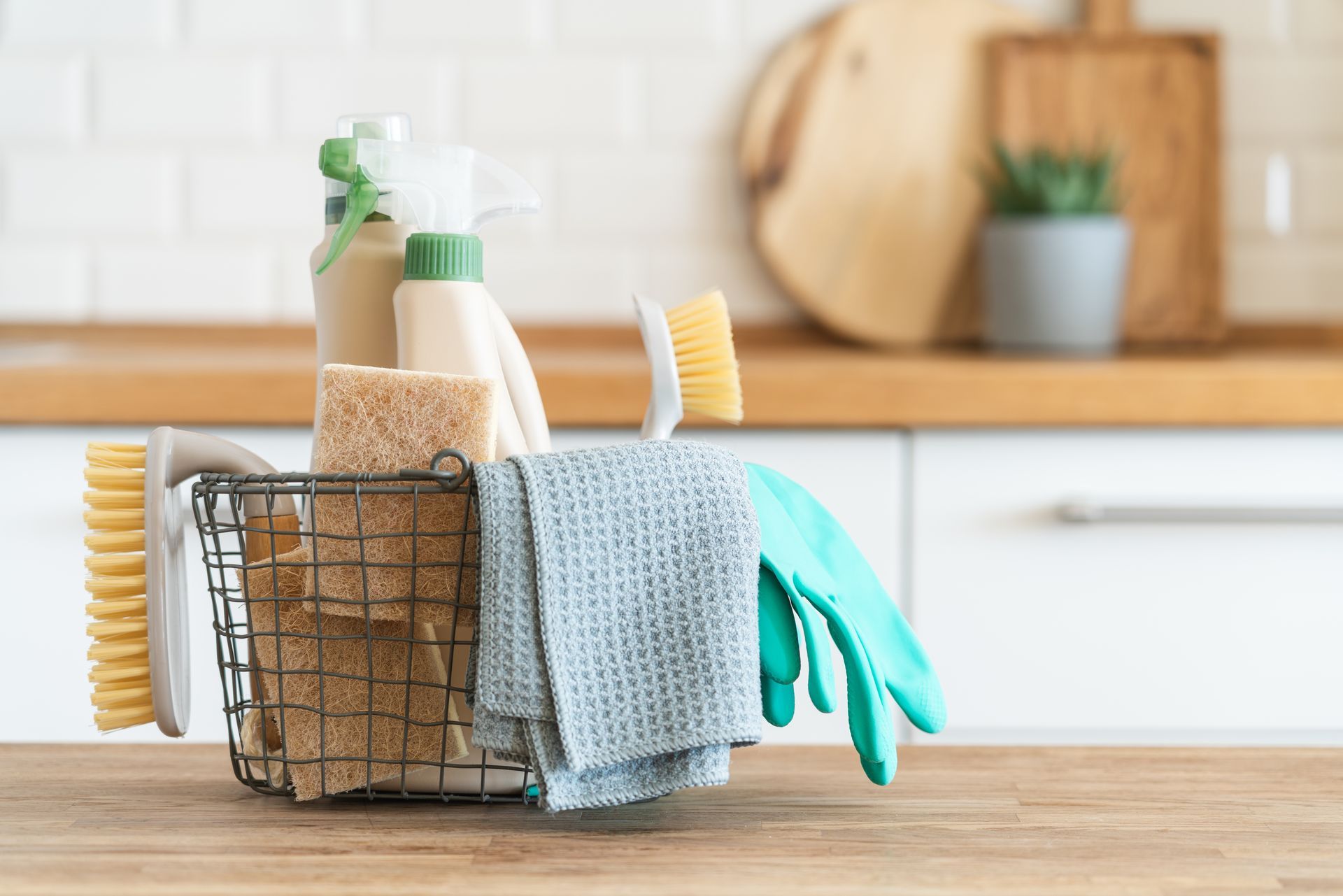 Produits d’entretien dans un panier métallique, avec des gants en caoutchouc et des chiffons sur un plan de travail de cuisine