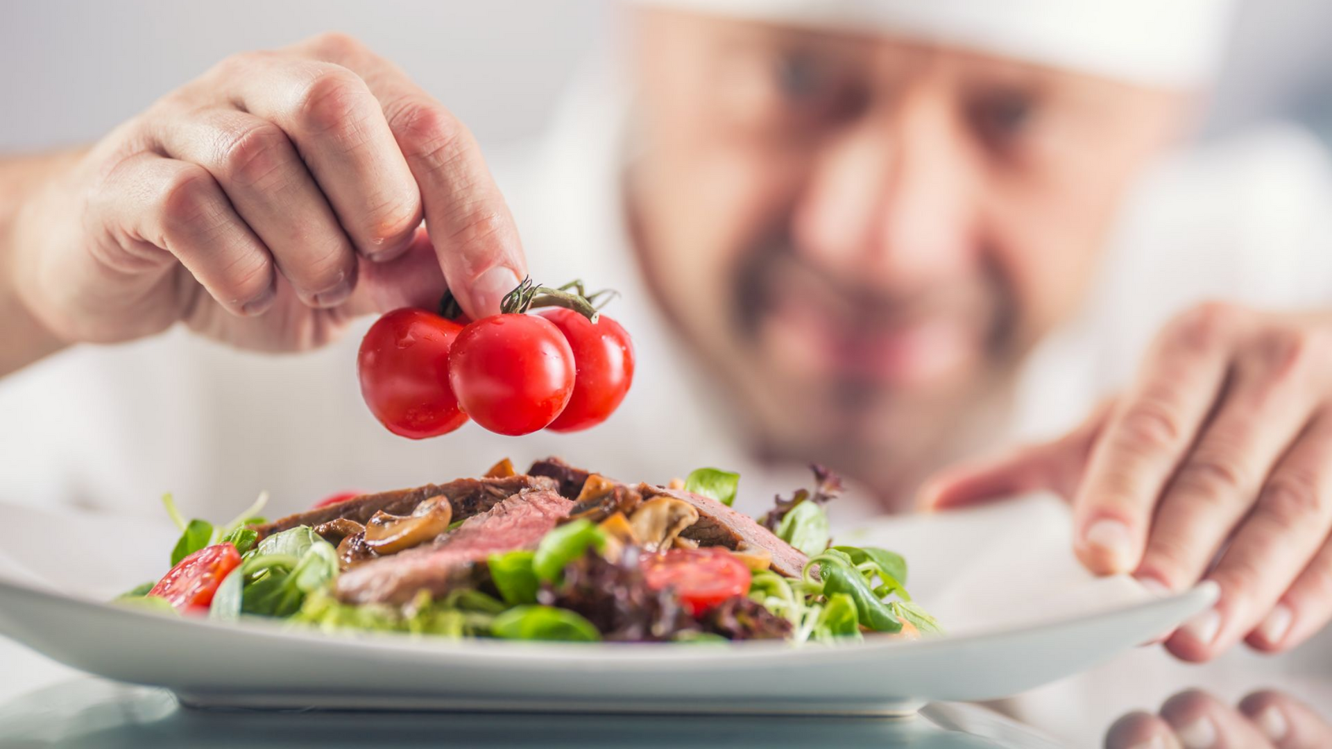 Un cuisinier dépose une grappe de 3 tomates cerise sur une salade.