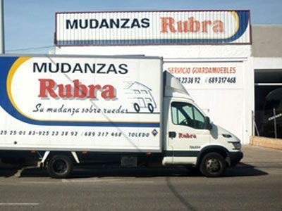 Un camión blanco está estacionado frente a un edificio que dice mudanzas rubra