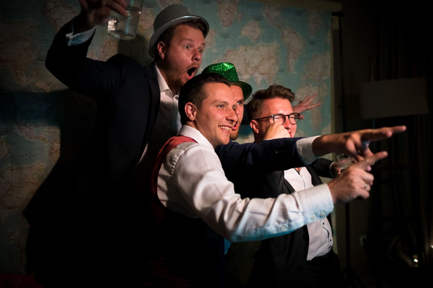 Cuatro hombres con sombreros y trajes posan frente a un fondo de mapas, uno señalando y el otro sonriendo.