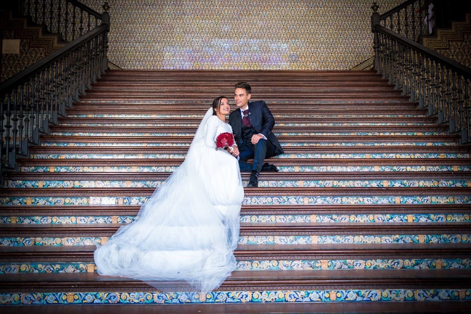 Recién casados ​​sentados en una escalera ornamentada. 