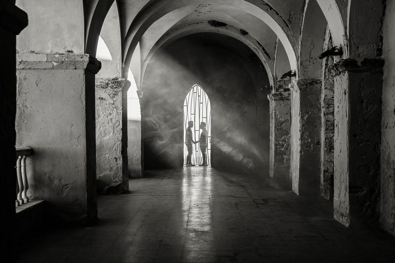 Pasillo arqueado, de piedra, con luz que entra a través de una ventana enrejada; se recorta una figura.