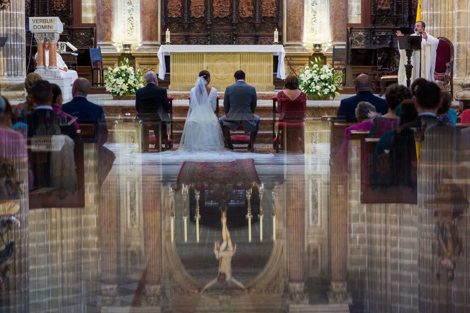 Ceremonia nupcial en una iglesia; los novios en el altar, los invitados sentados y el sacerdote hablando.