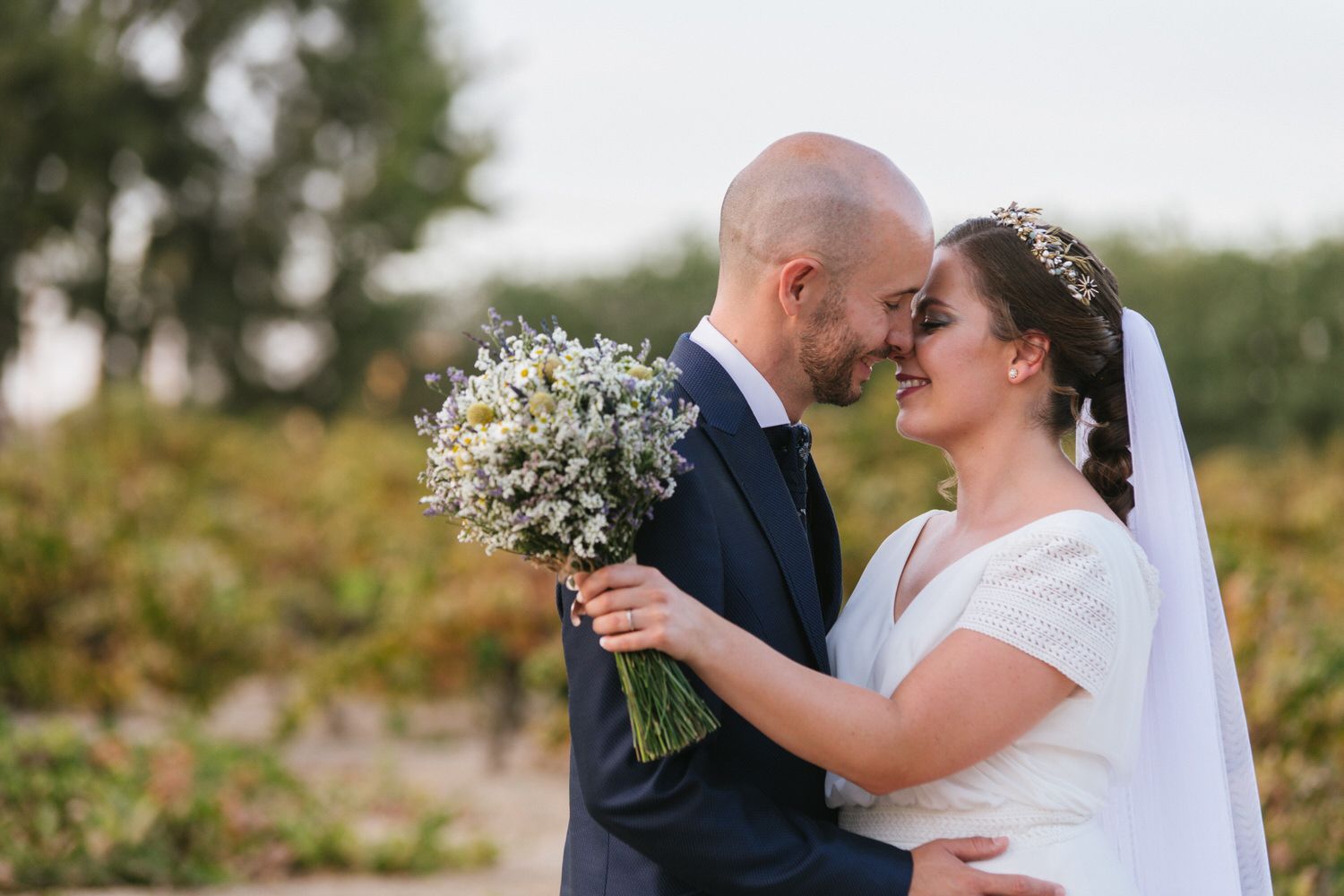 Los recién casados ​​se abrazan, el hombre sostiene flores. Al aire libre, un día soleado.