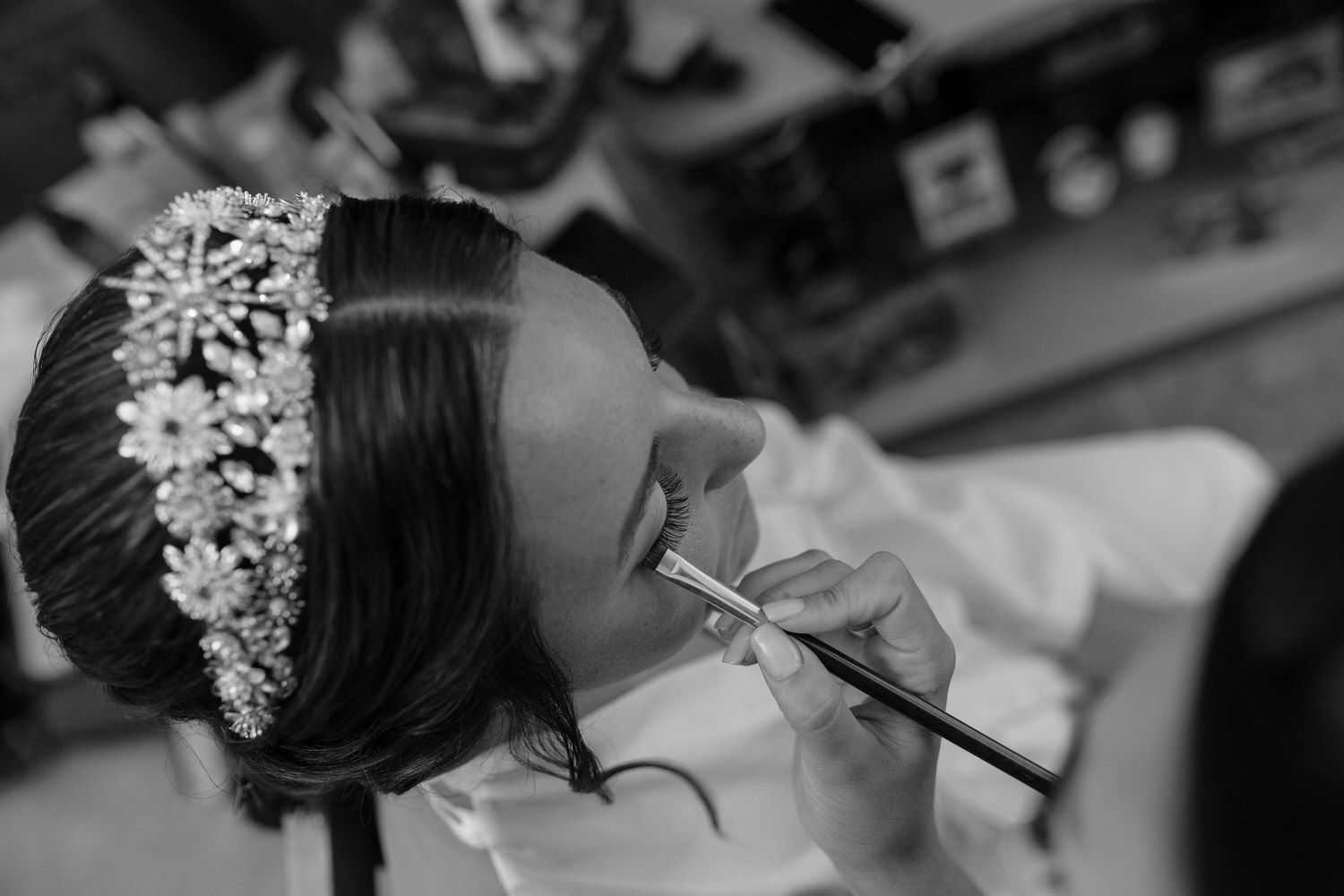 Mujer aplicándose lápiz labial con un pincel, luciendo una diadema con joyas.