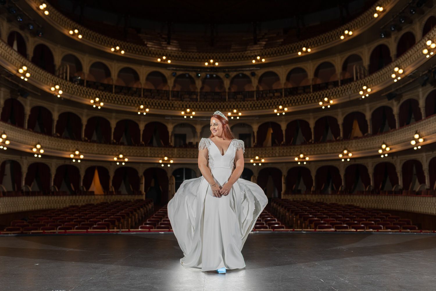 Mujer vestida de blanco en el escenario, fondo de teatro adornado.
