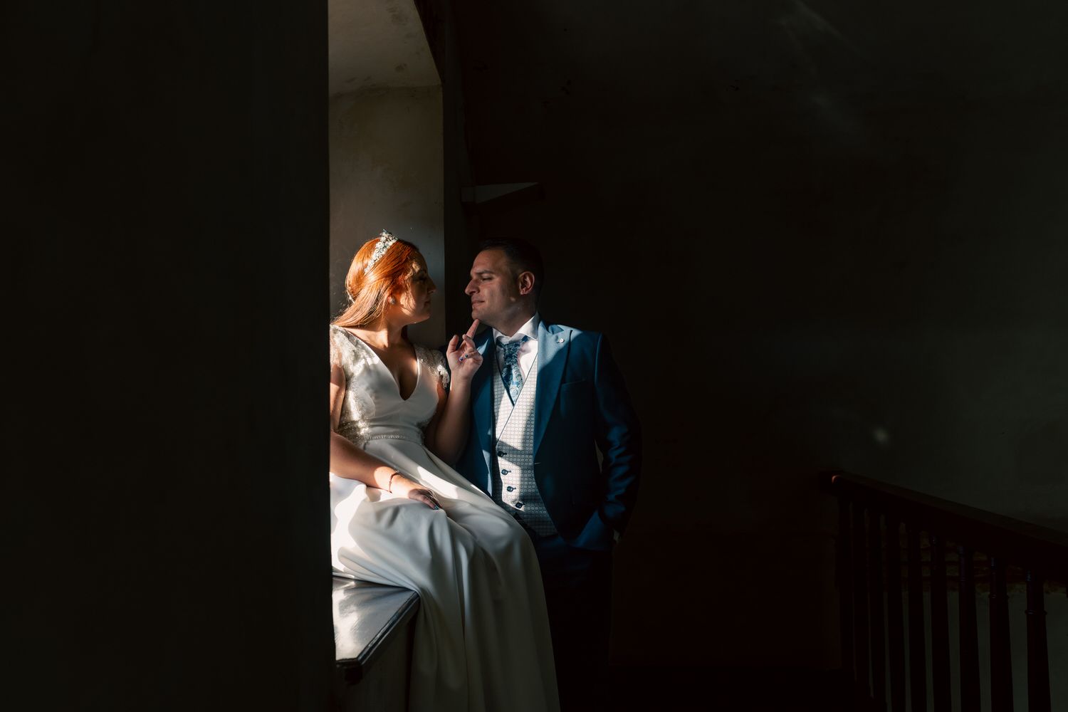 Novios en un interior oscuro, iluminados por una ventana. 
