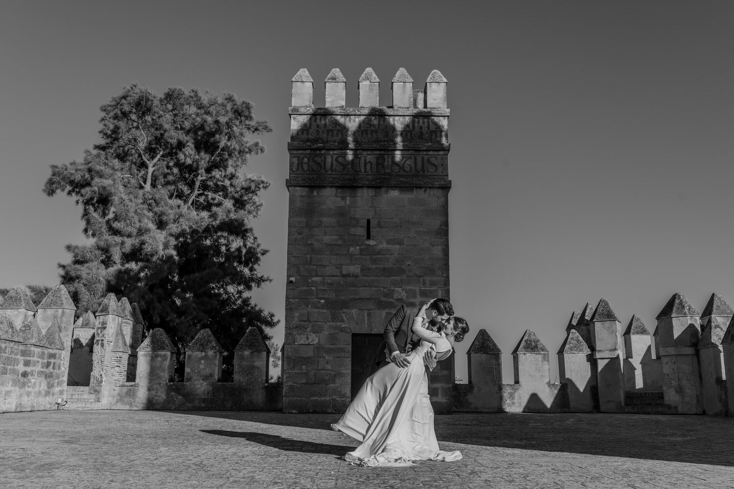 Los novios se abrazan frente a la torre de un castillo; fotografía en blanco y negro.