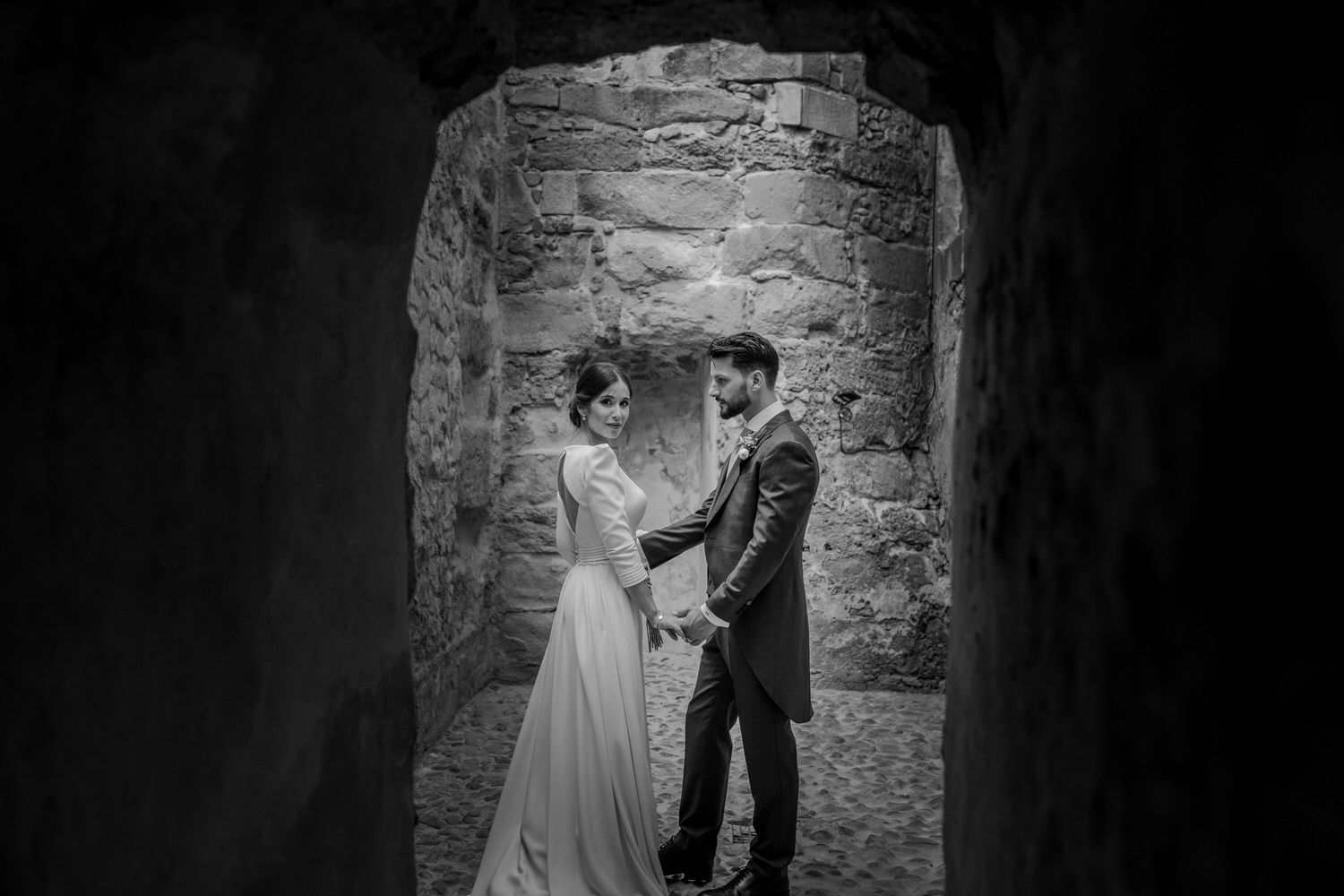 Novios tomados de la mano en un arco de piedra. Foto en blanco y negro.