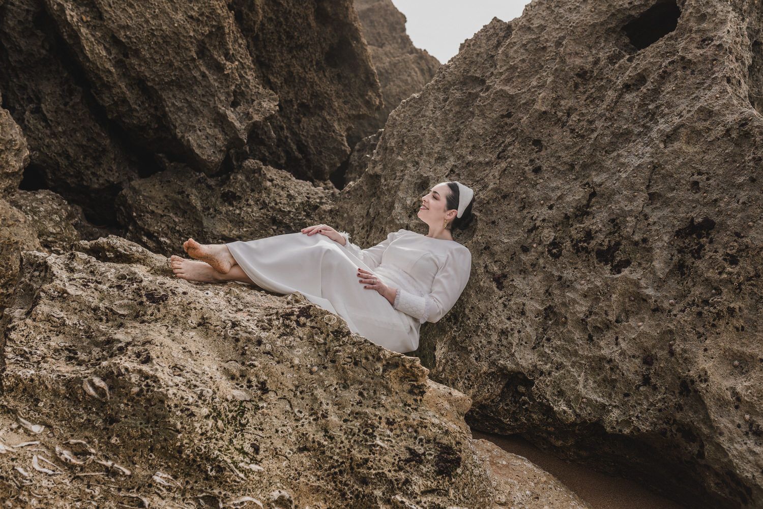 Mujer vestida de blanco se reclina sobre las rocas, mirando hacia arriba.