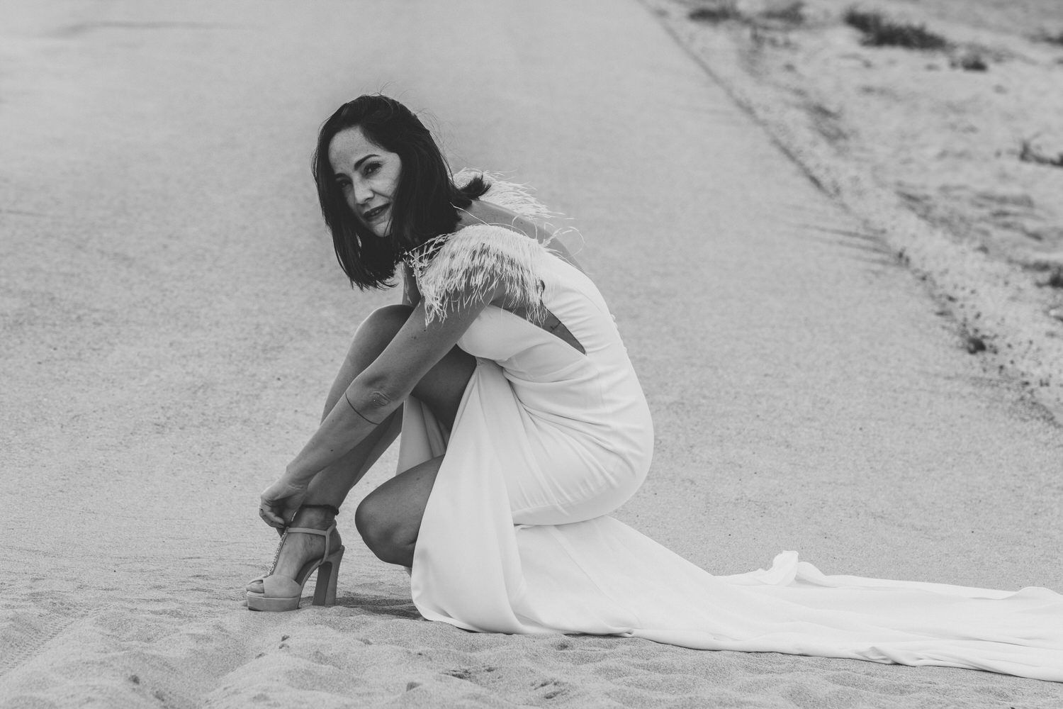 Una mujer con vestido de novia se pone en cuclillas y se ata el zapato