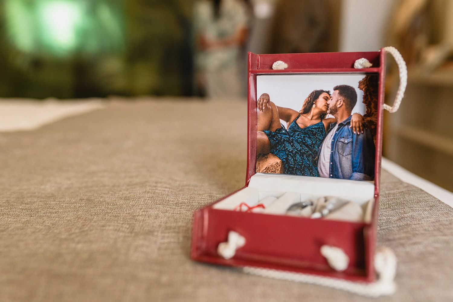 Joyero rojo con foto de pareja besándose, sobre una cama.