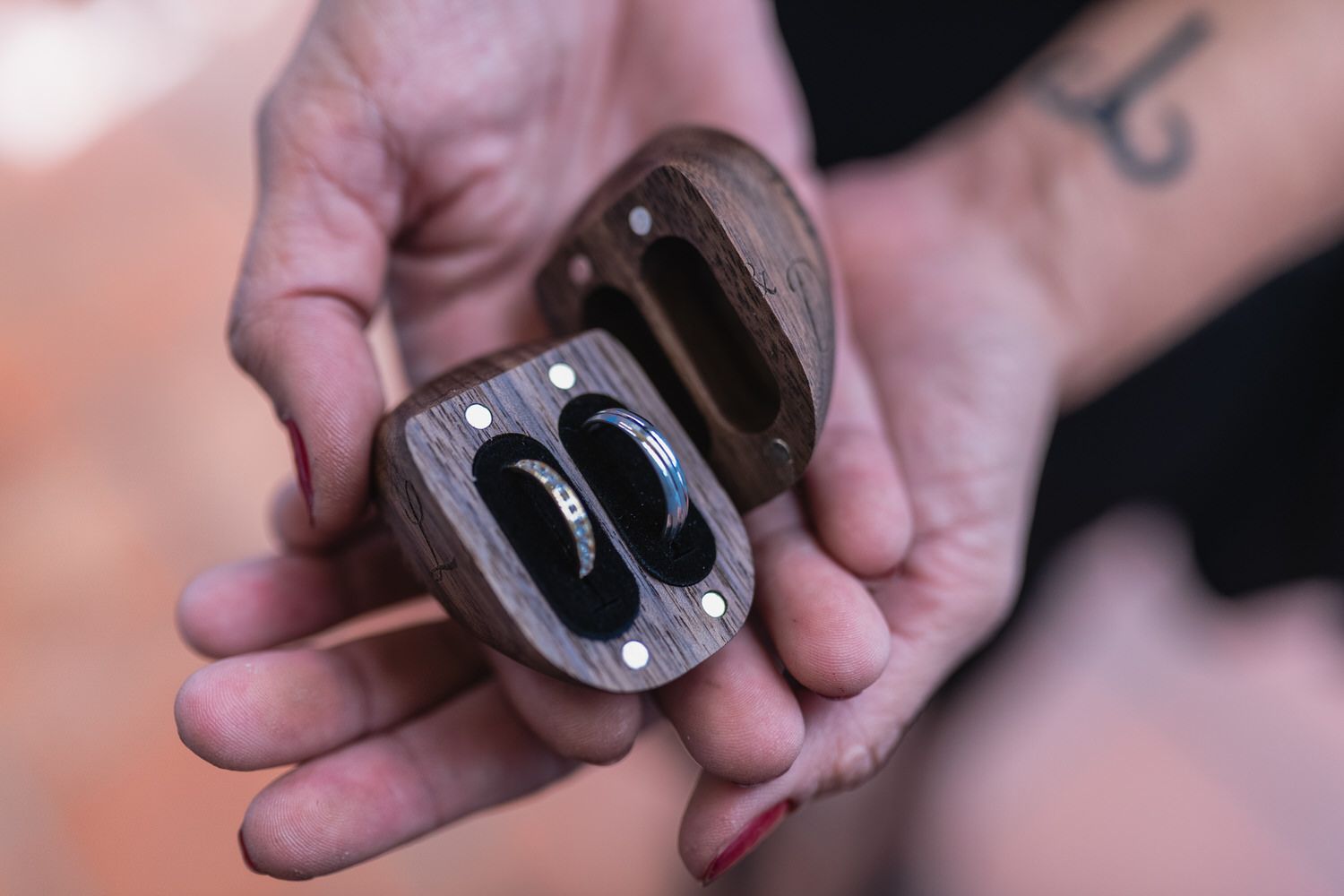 Manos sosteniendo una caja de madera abierta que contiene dos anillos; primer plano.