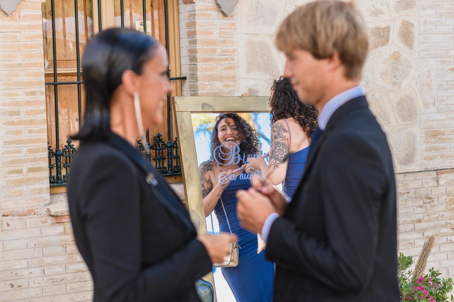 Gente conversando, reflejo en el espejo de una mujer en azul, fondo de edificio de piedra.