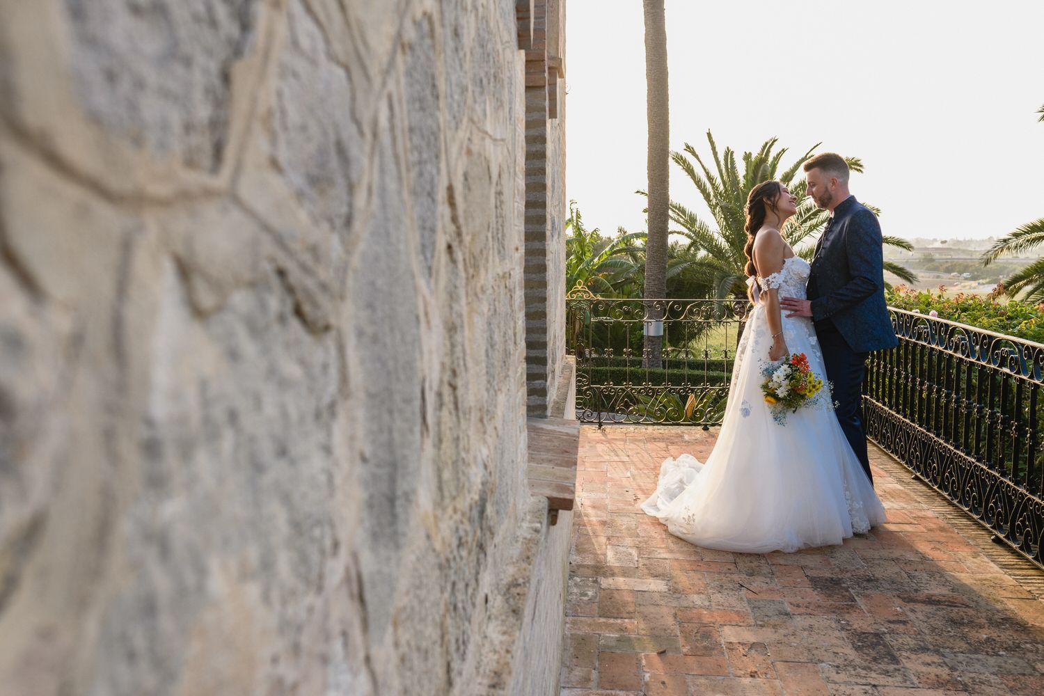 Los novios se abrazan en un patio de ladrillo. Ella lleva un vestido blanco, él un traje azul marino. 