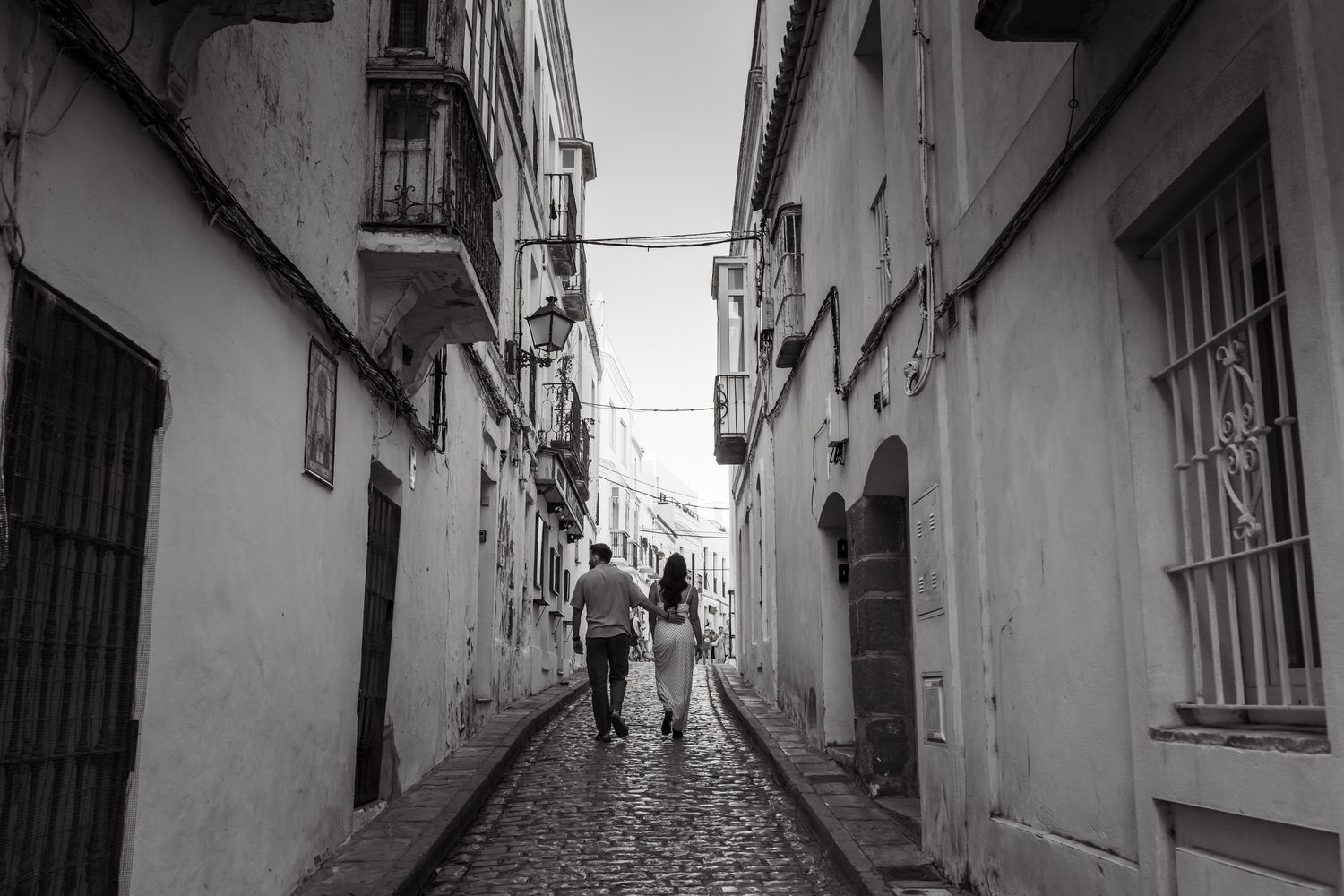 Pareja caminando por una calle adoquinada entre edificios antiguos, en blanco y negro.