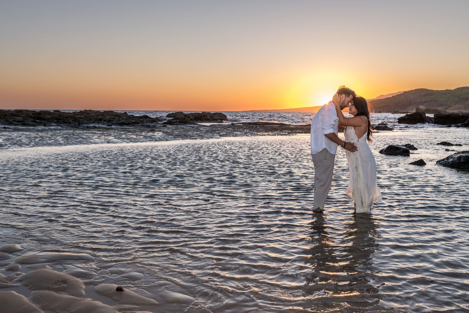 Pareja abrazándose en aguas poco profundas al atardecer.