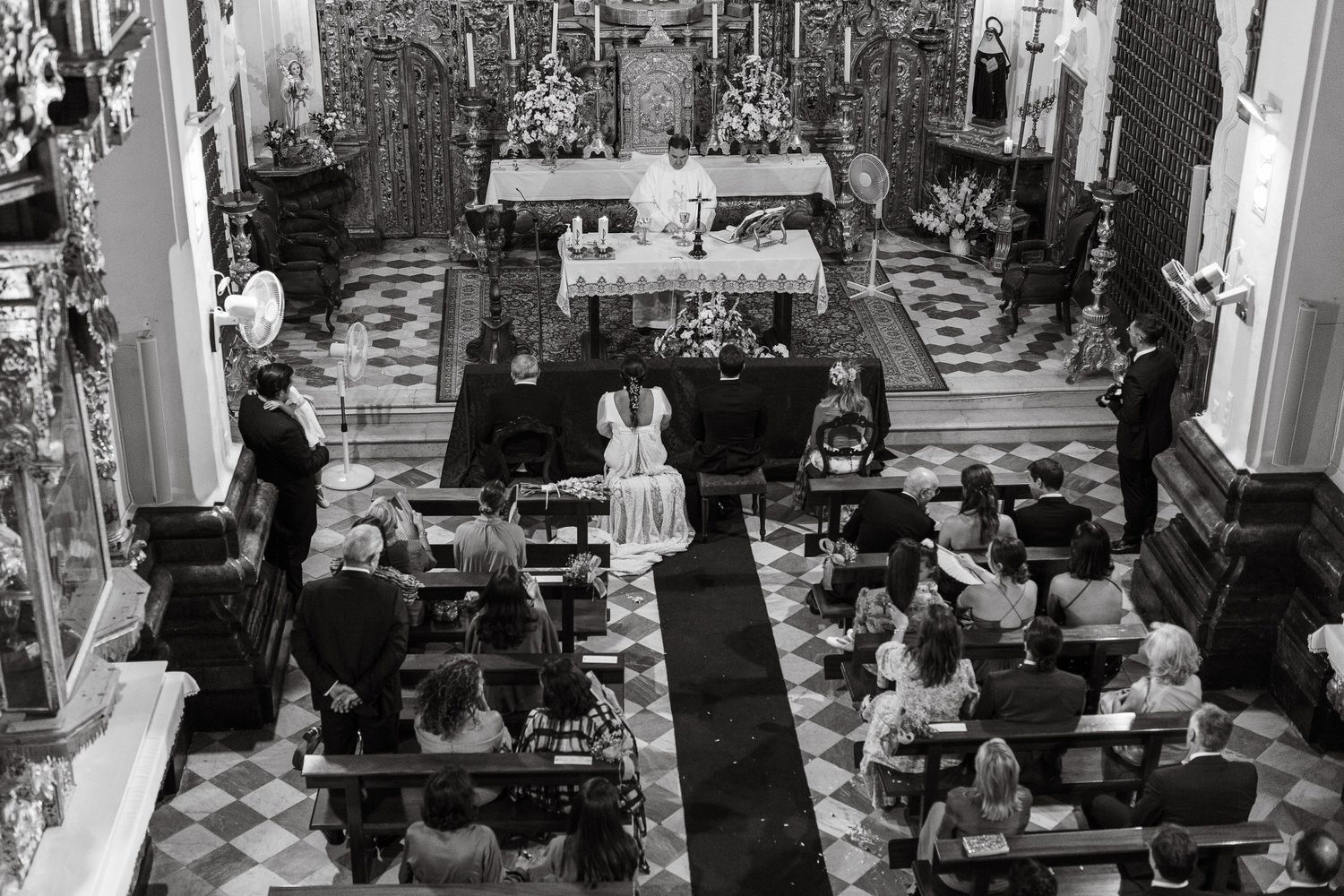Ceremonia de boda en una iglesia: los novios en el altar, los invitados sentados en los bancos, blanco y negro.
