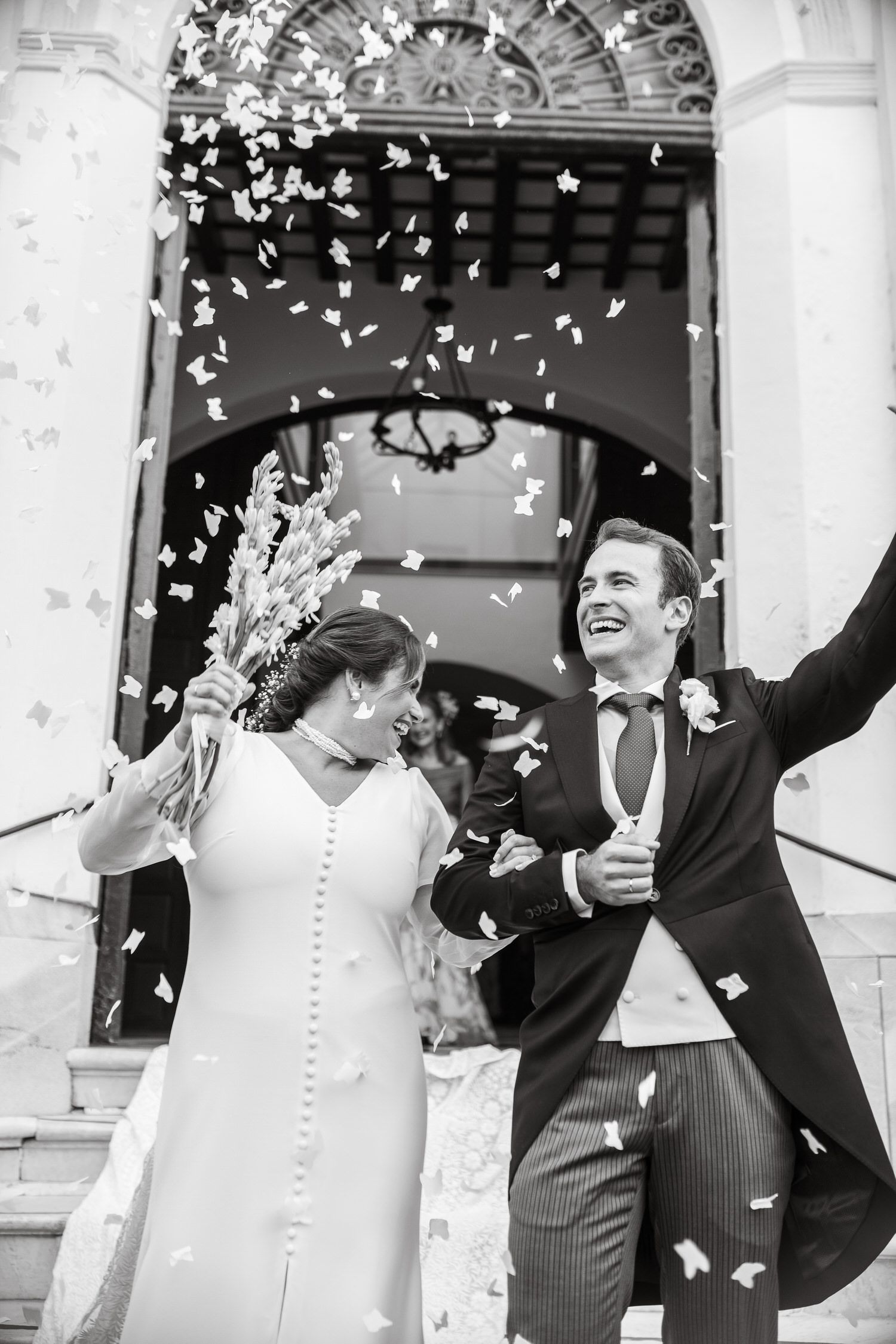 Novios saliendo de un edificio, con confeti cayendo. Ambos sonriendo y alzando los brazos en señal de celebración.