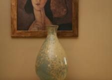 Un jarrón está sobre una mesa delante de un cuadro de una mujer.