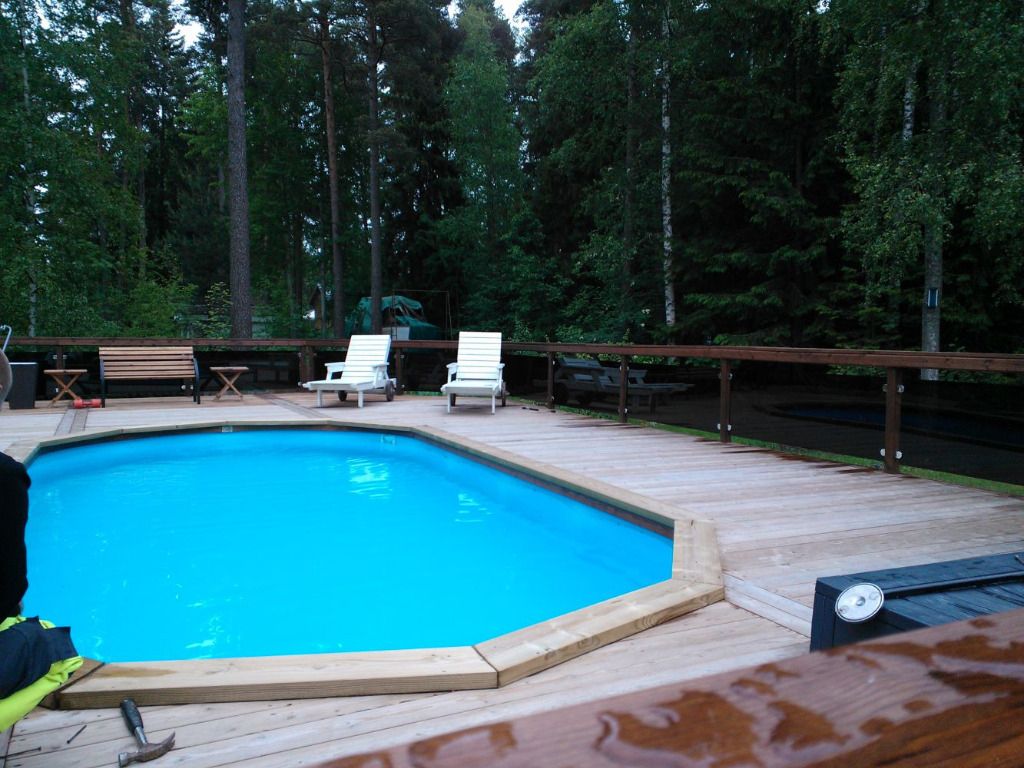 Uima-allas kahdella valkoisella tuolilla puisella terassilla metsän edessä.