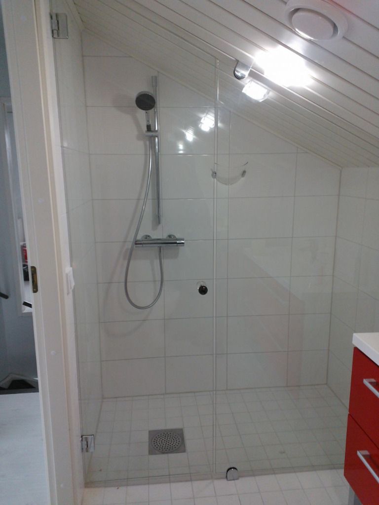 Suihkukaappi lasiovella, valkoisilla laatoitetuilla seinillä ja viistolla katolla.