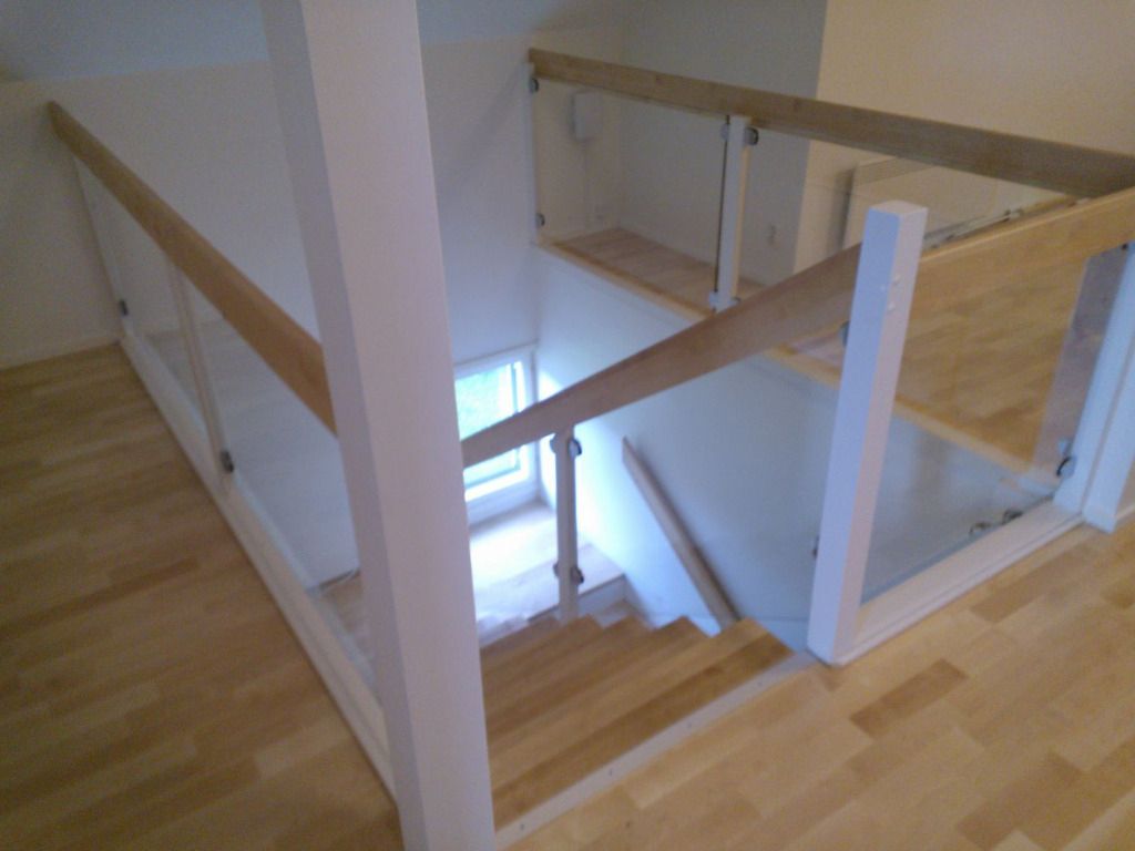 Puinen portaikko lasilla ja puukaiteella; valkoiset seinät.