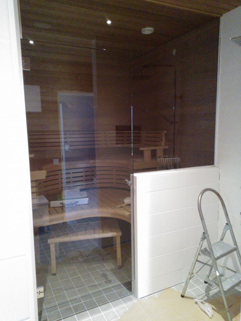 Sauna, jossa on lasiovi, puiset penkit ja puupaneloidut seinät. Sivussa on askeltikkaat.