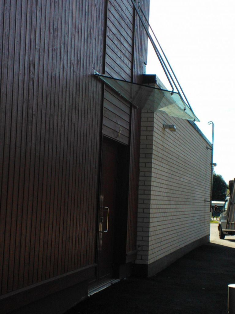 Sivukuva ruskeasta rakennuksesta, jossa on tiiliseinä ja lasimarkiisilla varustettu ovi.