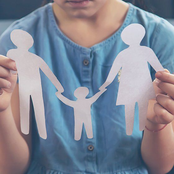 Enfant tenant entre ses doigts des petits bonhommes de papier représentant une famille