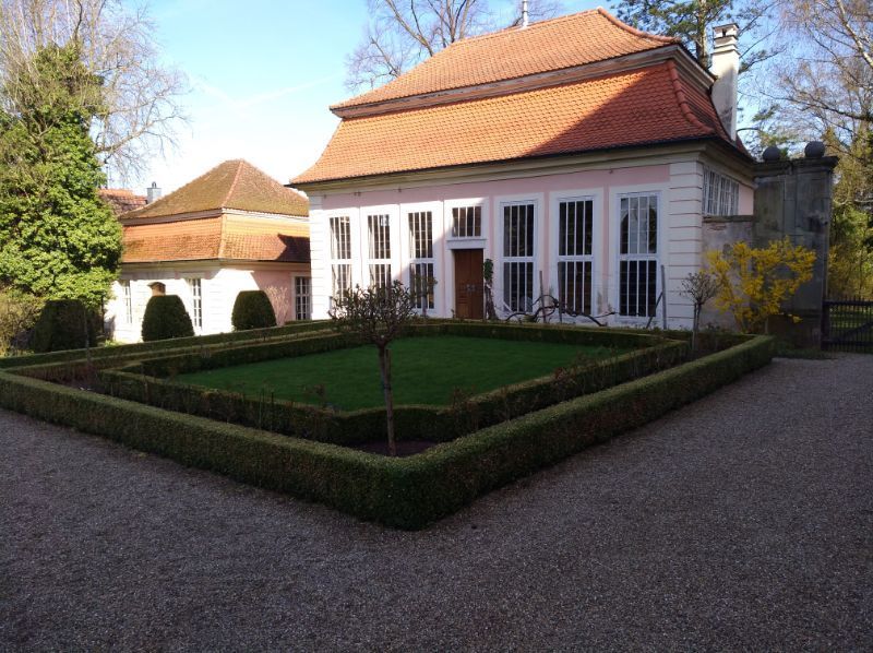 quadratische kunstvoll gestaltete Grünfläche vor einem Haus mit rotem Dach