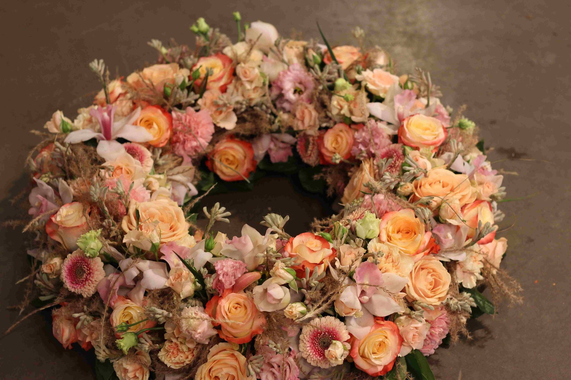 Kranz aus pfirsichfarbenen und rosa Rosen und anderen Blumen auf dunklem Untergrund.