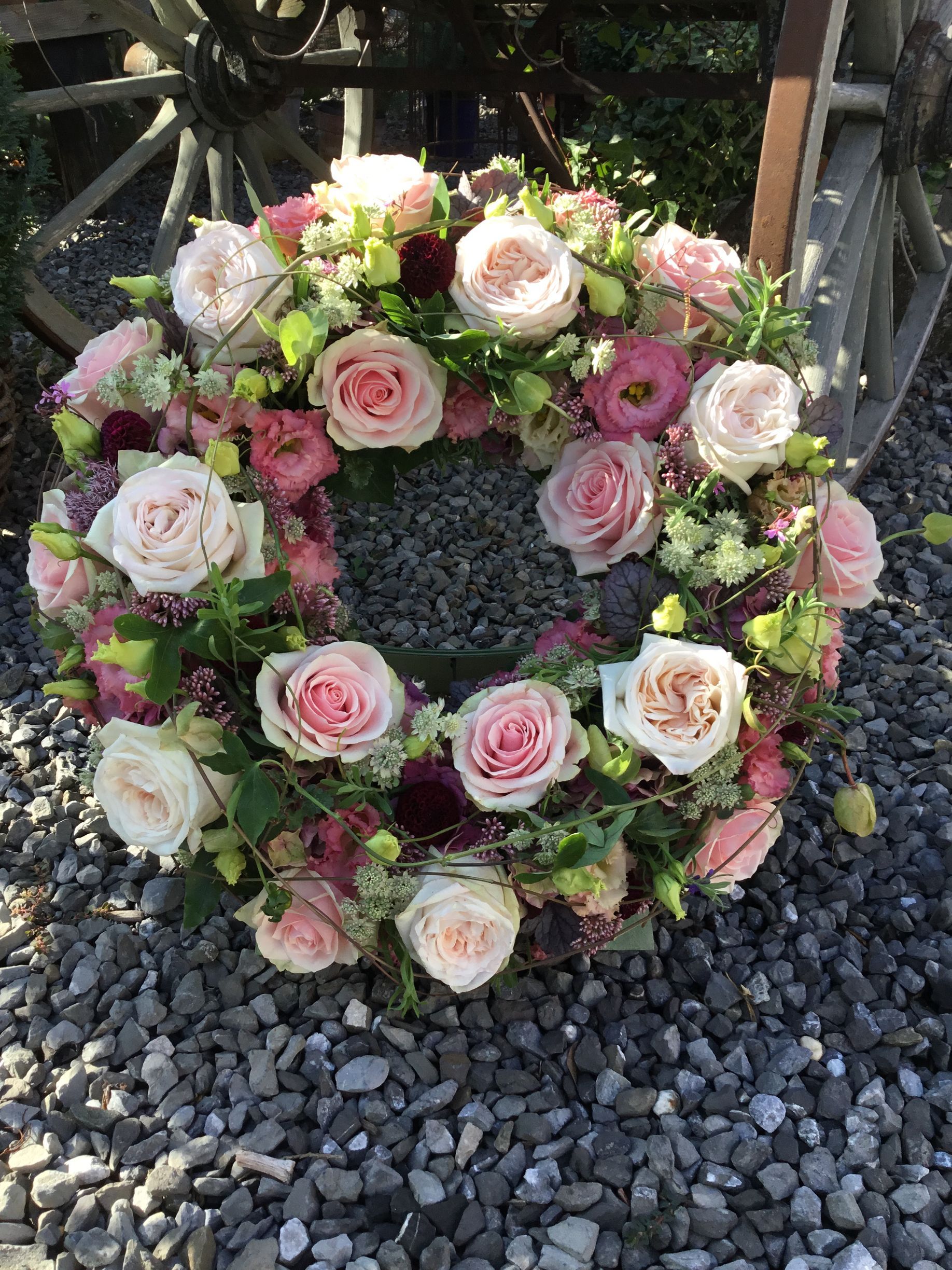 Blumenkranz aus rosa und weißen Rosen auf einem Bett aus grauen Kieselsteinen.