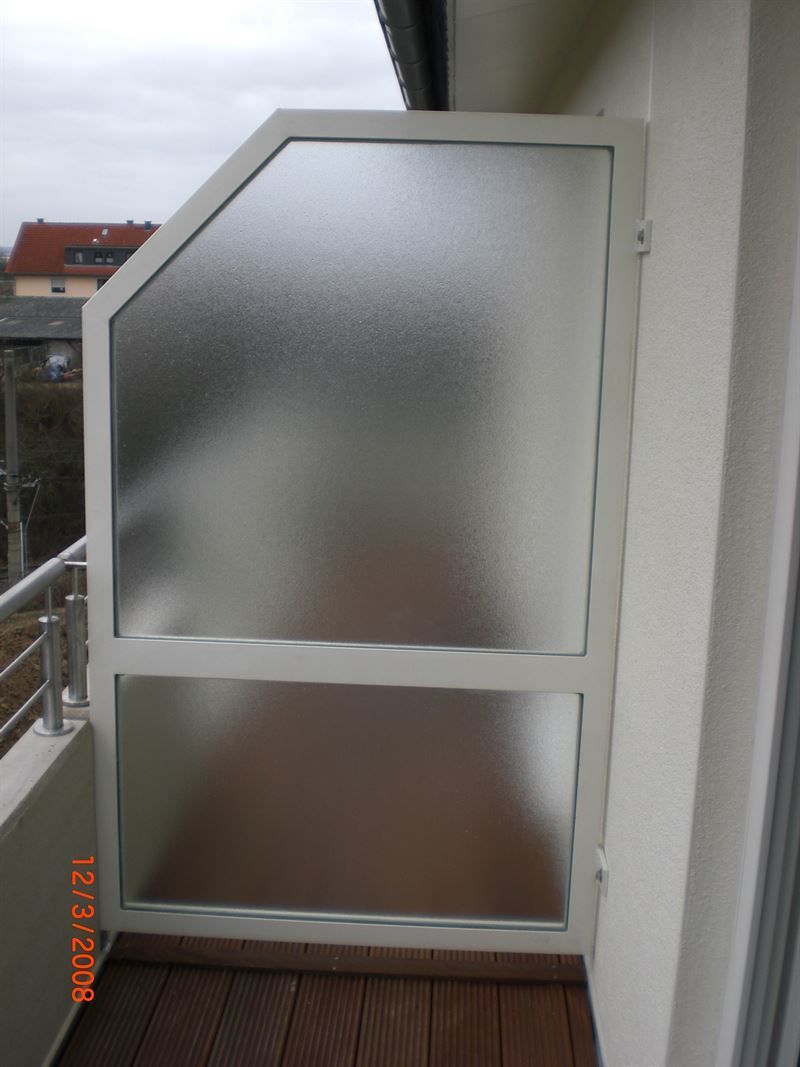 Ein Balkon mit Milchglastrennwand und Holzboden.