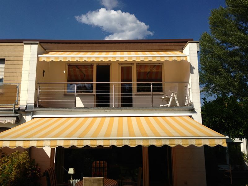 Ein Balkon mit einer gelb-weißen Markise darüber