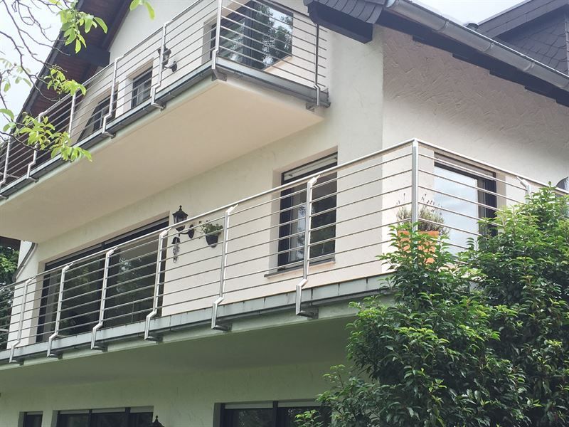 Ein weißes Haus mit Balkon und Edelstahlgeländer