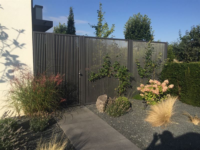 In einem Garten ist ein Holzzaun von Pflanzen und Steinen umgeben.