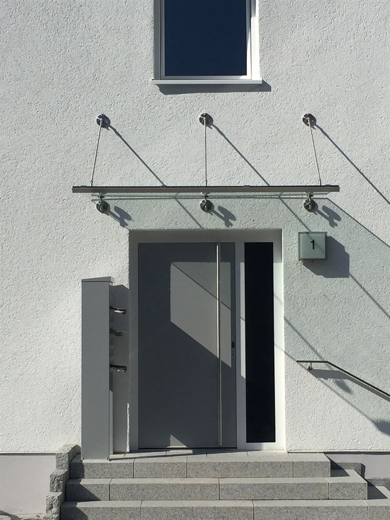 Ein weißes Gebäude mit einem Glasdach über der Tür und der Treppe.