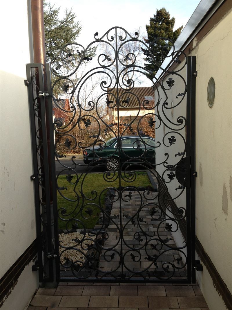 Ein schmiedeeisernes Tor führt zu einer Einfahrt, im Hintergrund ist ein Auto geparkt.
