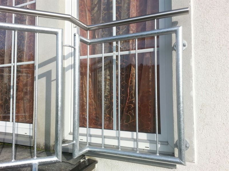 Neben einem Fenster an der Seite eines Gebäudes befindet sich ein Edelstahlgeländer.
