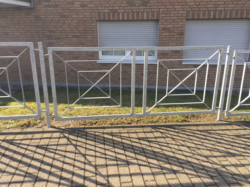 Auf dem Gehweg vor einem Backsteingebäude steht ein Metallzaun.