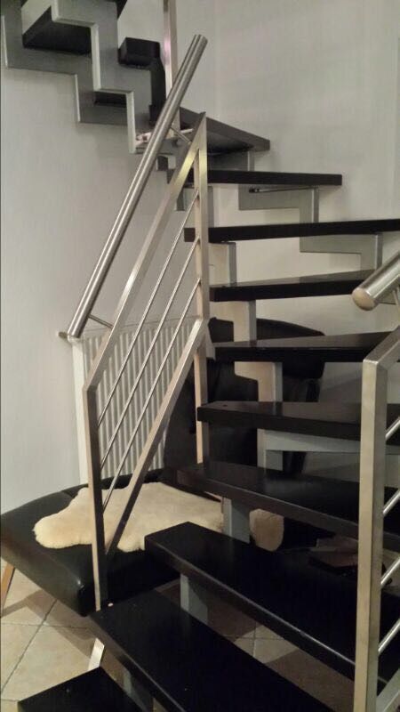 Eine Treppe mit schwarzen Stufen und einem Edelstahlgeländer