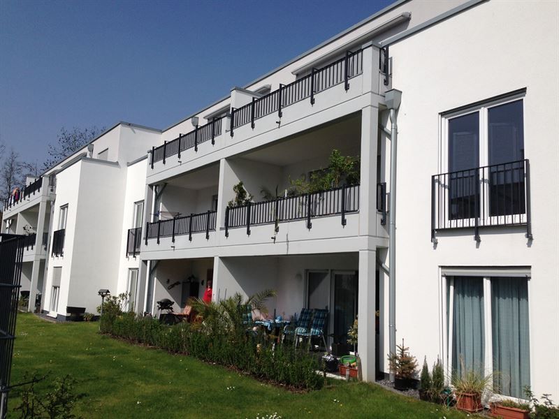 Ein weißes Mehrfamilienhaus mit Balkonen und einer Wiese davor